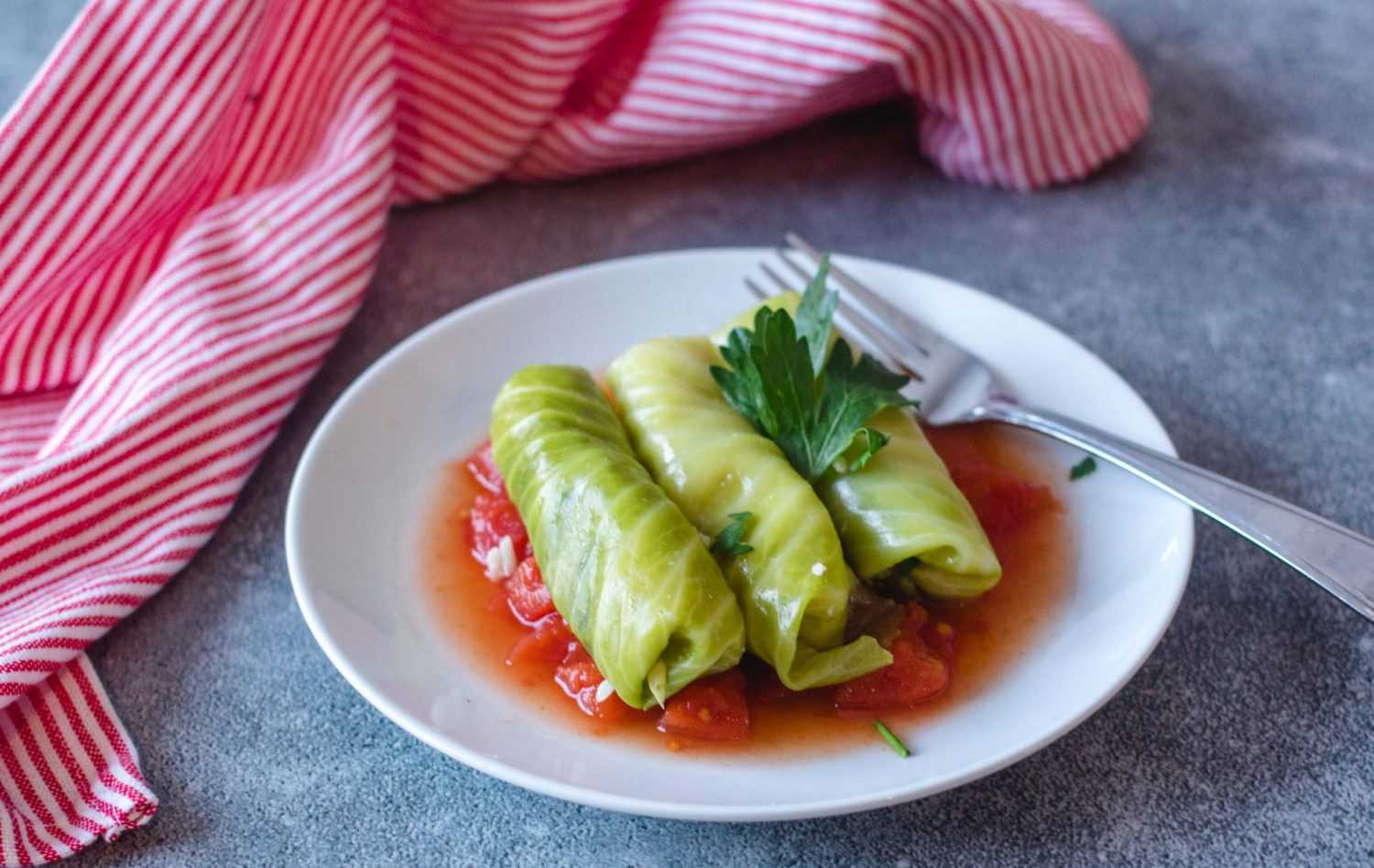 Cabbage rolls in red sauce topped with chopped parsley on white plate