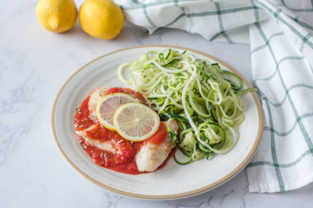 Cod fillets in marinara sauce topped with lemon slices and zucchini noodles on side