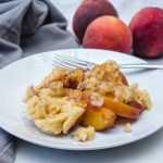 peach cobbler in a plate with fork and whole peaches on side