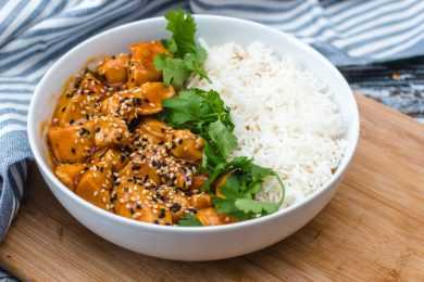 Chicken cubes in brown sauce topped with black and white sesame alongside white rice and parsley