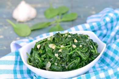cooked spinach in a white bowl topped with minced garlic with spinach leaves on side