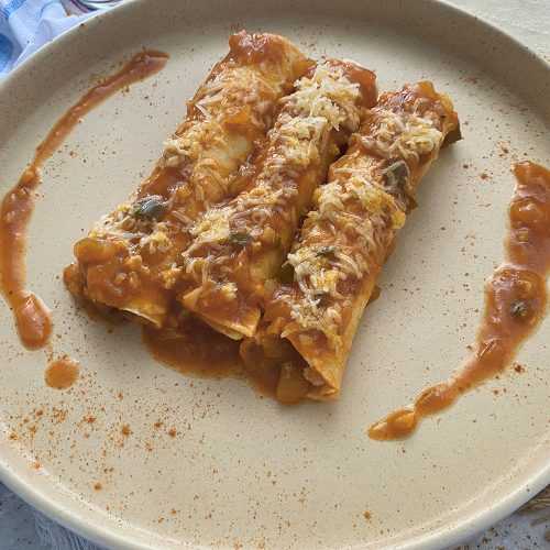 Three chicken enchiladas topped with red sauce and melted cheese on white plate