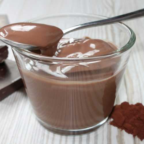 Glass filled with chocolate pudding with spoon with pudding and chocolate cubes on side