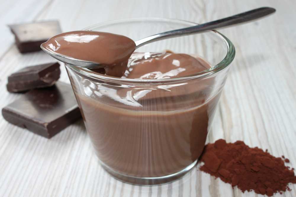 Glass filled with chocolate pudding with spoon with pudding and chocolate cubes on side