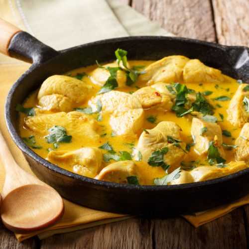 Chicken cubes in curry paste, turmeric and coconut milk with parsley on top in black pan