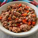 Ground beef mixed with chopped bell pepper, minced onion and garlic and parsley in tomato sauce in white bowl