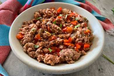Ground beef mixed with chopped bell pepper, minced onion and garlic and parsley in tomato sauce in white bowl