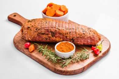 Pork sirloin on cutter board with slices carrots, sauce and rosemary on side