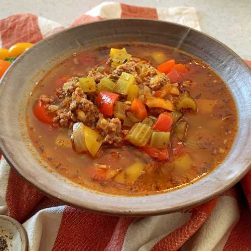 Red soup filled with ground beef, orange and red bell peppers, chopped onions and chopped celery