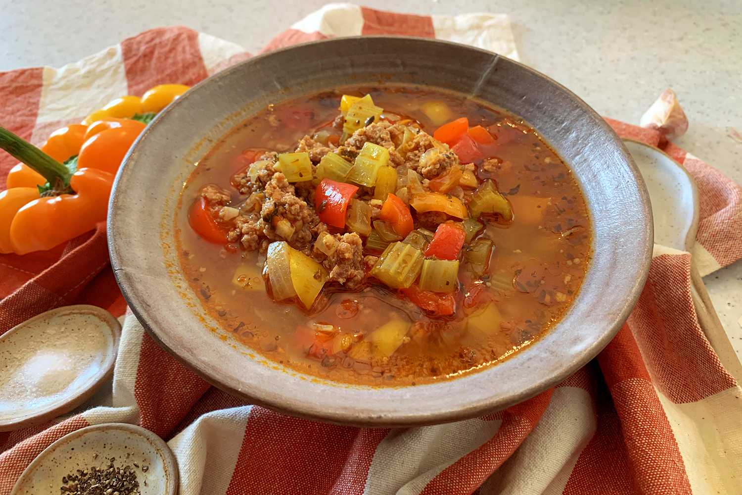 Red soup filled with ground beef, orange and red bell peppers, chopped onions and chopped celery