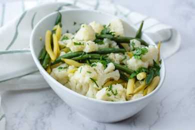 Steamed cauliflower florets, green bean and yellow been and a bowl topped which chopped parsley