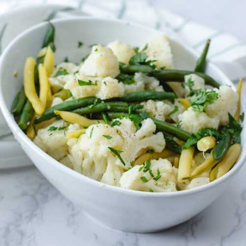 Steamed cauliflower florets, green bean and yellow been and a bowl topped which chopped parsley