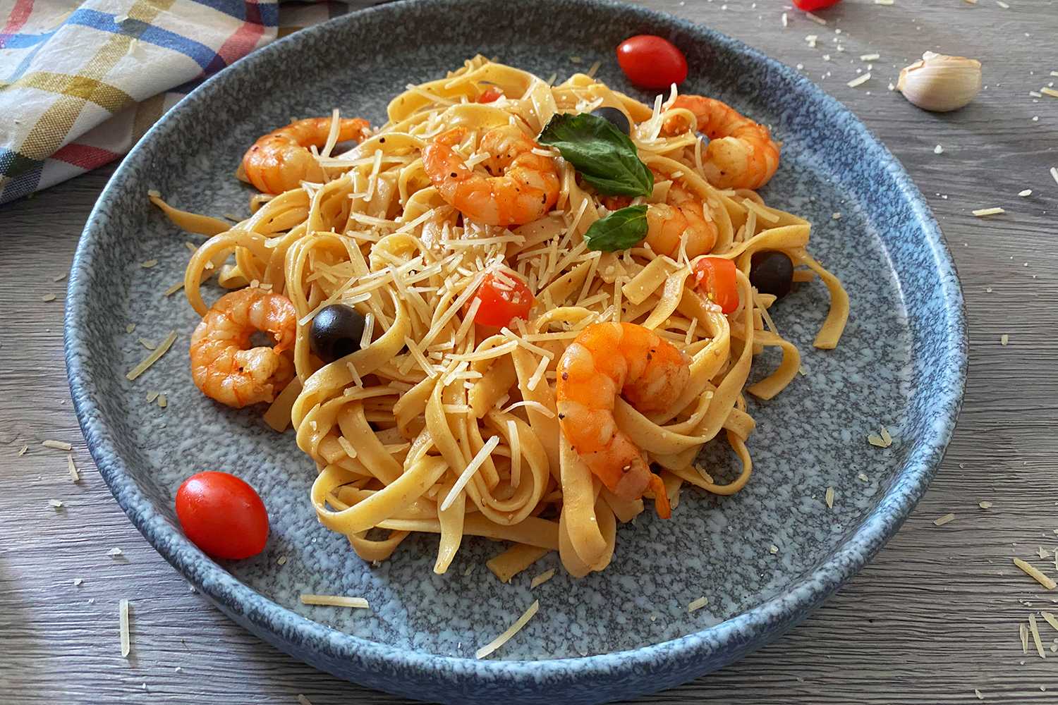 Cooked fettuccine noodles mixed with shrimp, black olives, cherry tomatoes and melted cheese on top