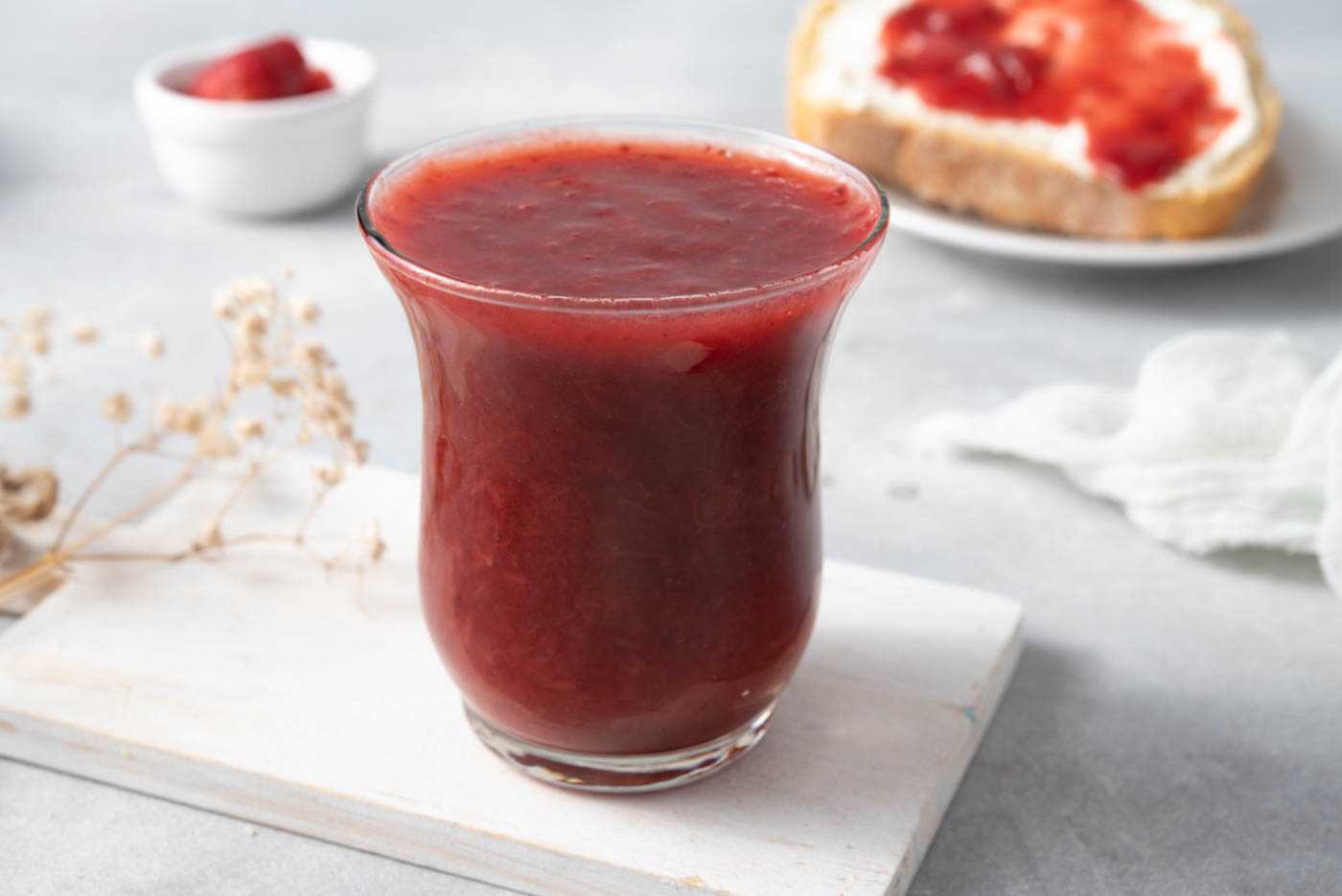 Strawberry jam in high glass with a bread with butter and jam on side