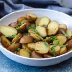 Halved red potatoes with skin topped with parsley, salt and pepper in white bowl