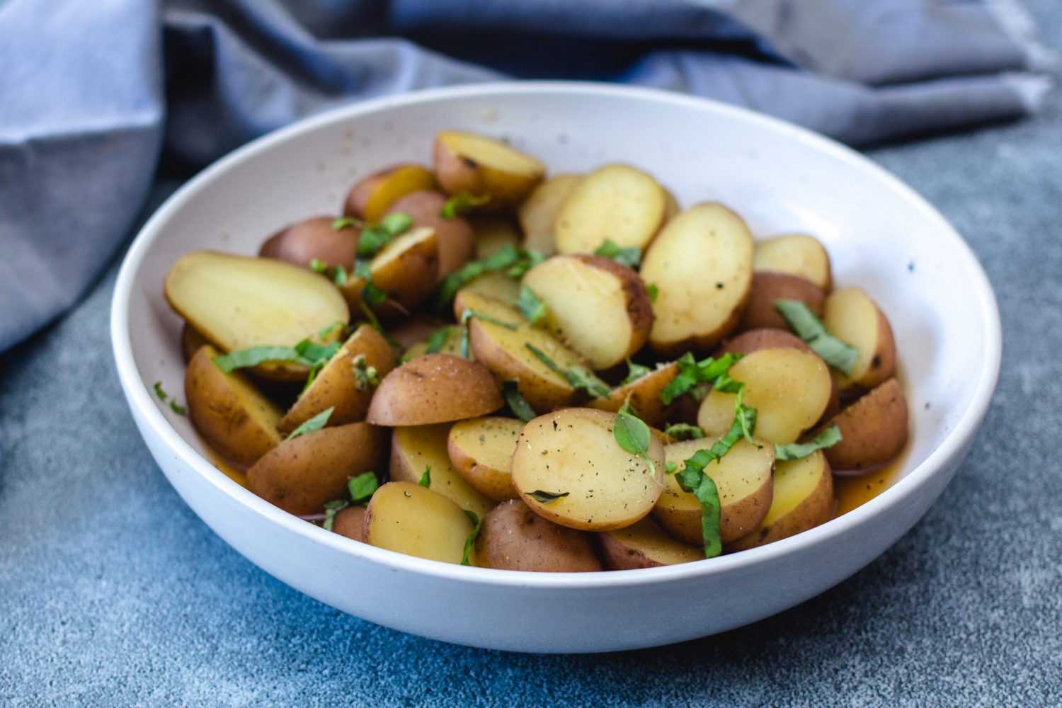 Halved red potatoes with skin topped with parsley, salt and pepper in white bowl