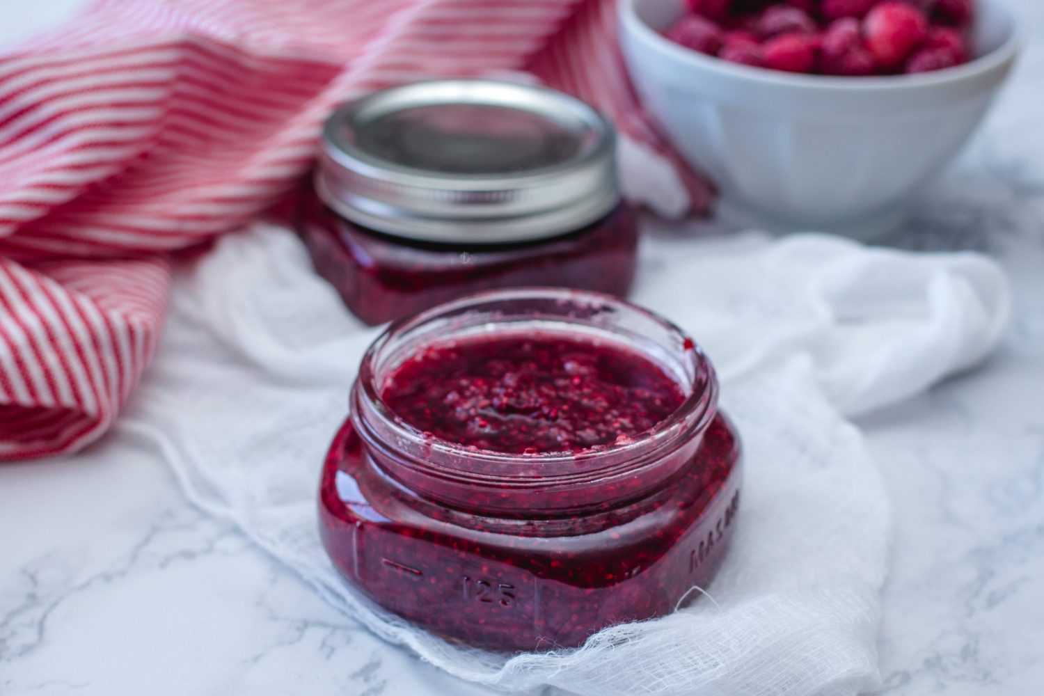 Purple raspberry jam inside an open jar and fresh raspberries on side