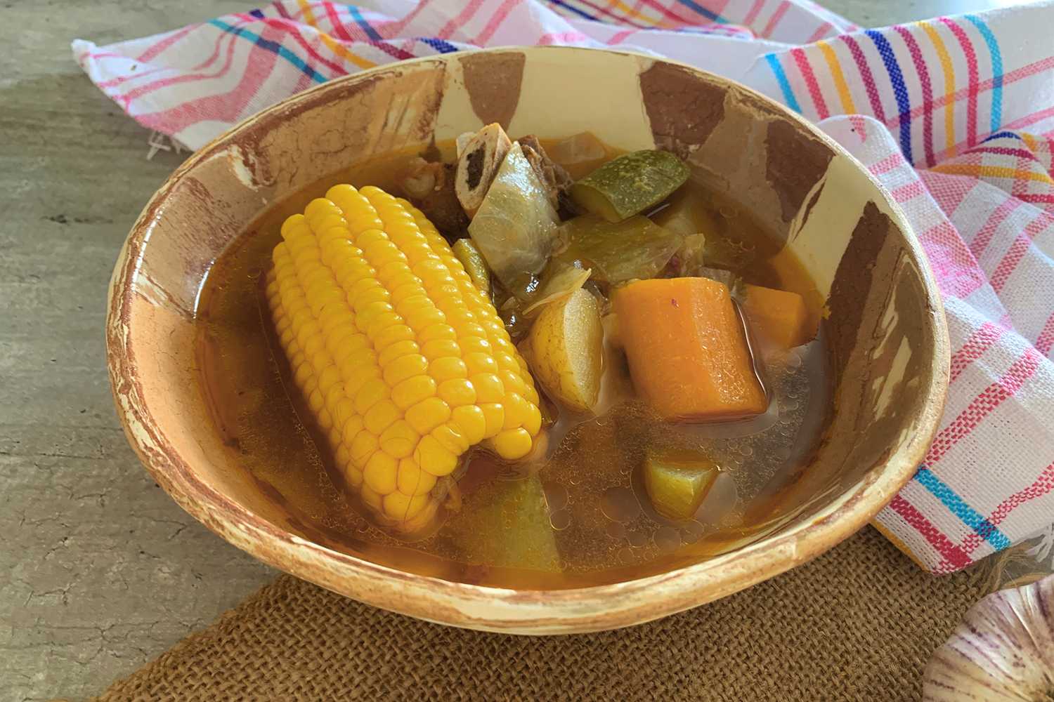 Clear soup with corn ear, beef chunks and chopped carrot and zucchini in brown bowl