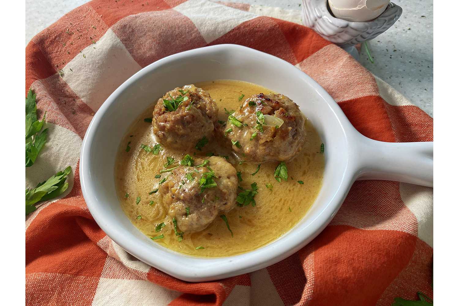 Three big meatballs in yellow sauce with chopped parsley on top in white bowl with handle