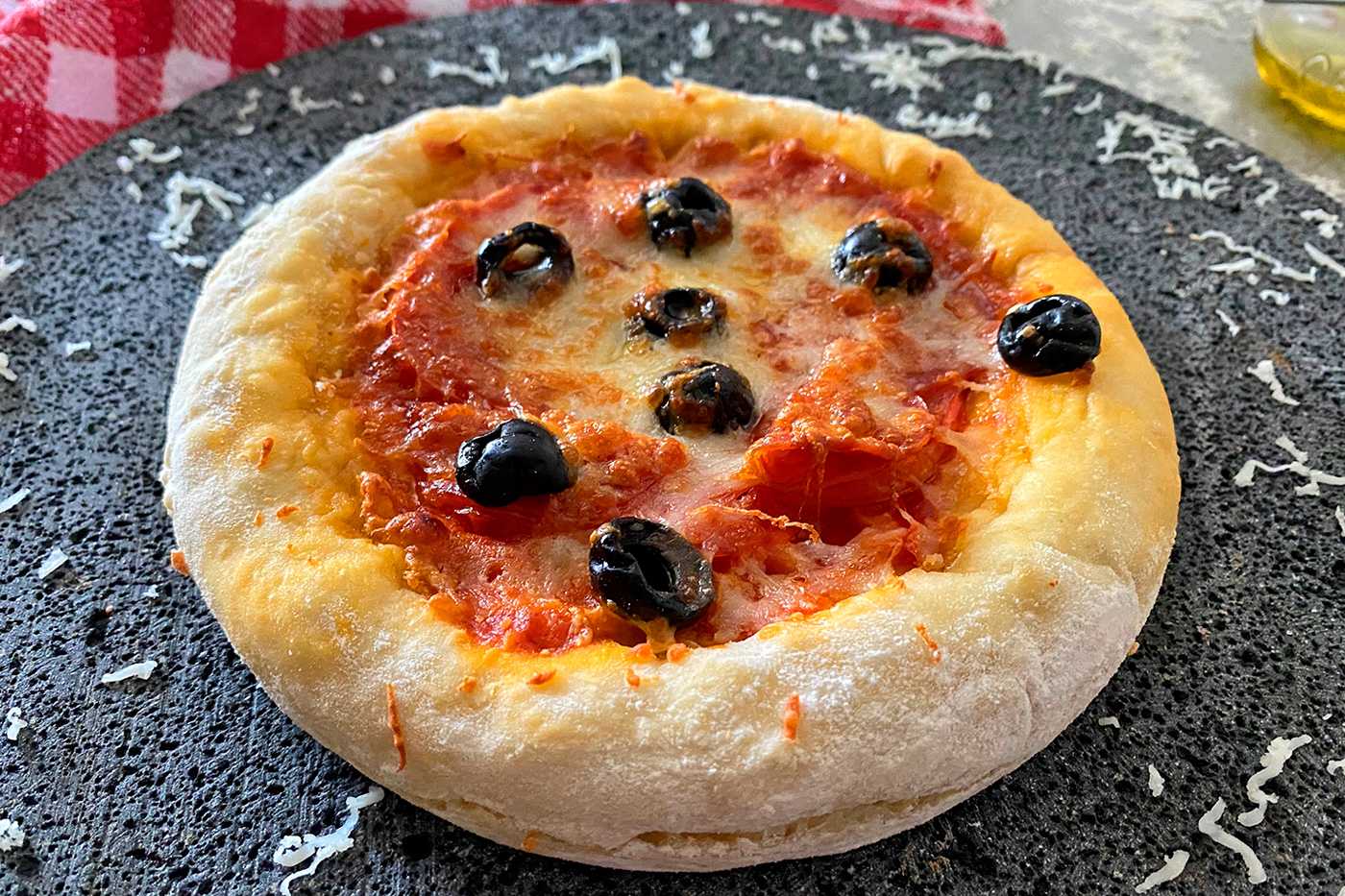 Small pizza with mozzarella cheese and tomato sauce topped with black olives on black plate