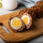 Ready to eat scotch eggs coated with sausage crust on a wooden cutter
