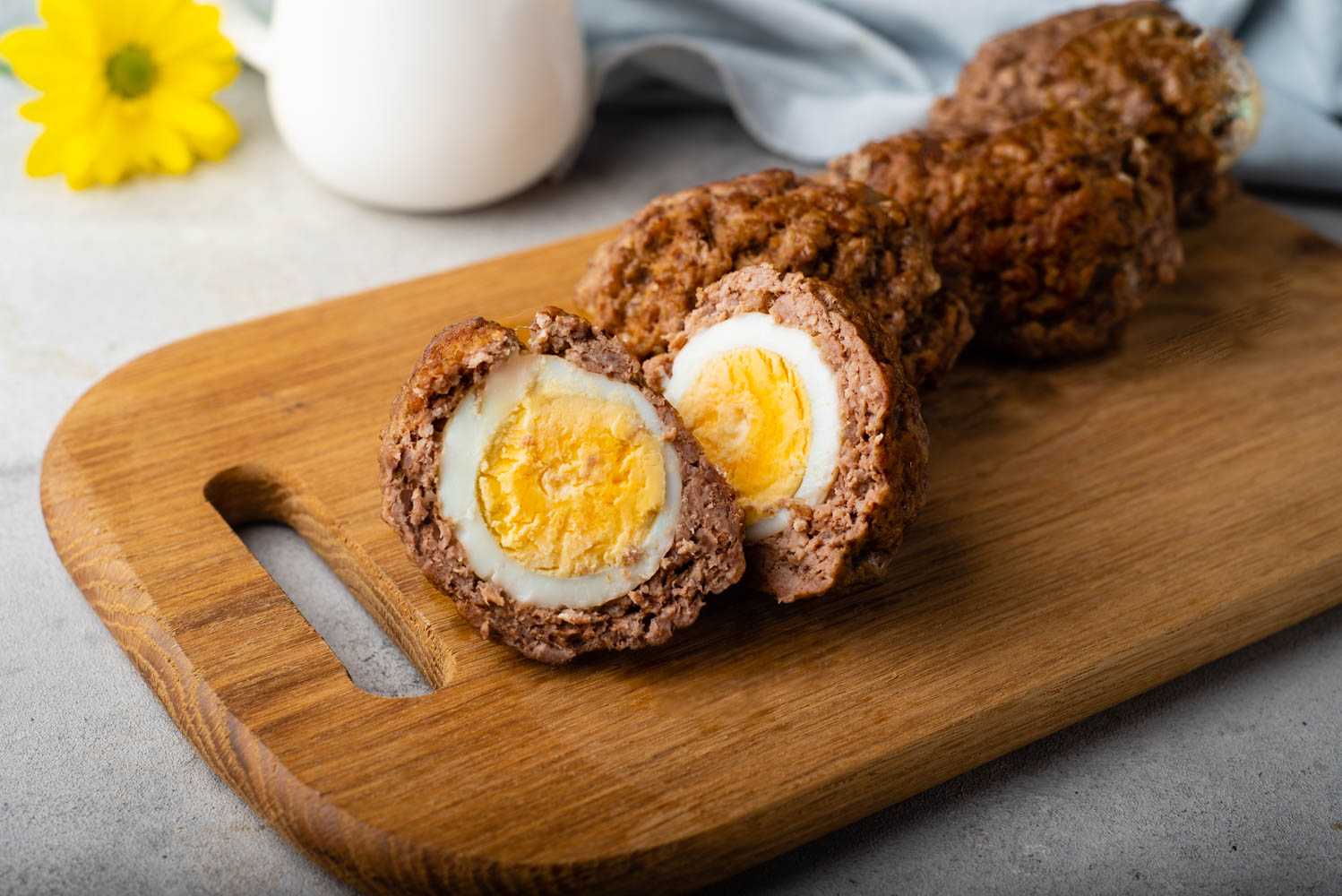 Ready to eat scotch eggs coated with sausage crust on a wooden cutter