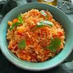yellow rice in tomato sauce topped with parsley leaves in a blue plate