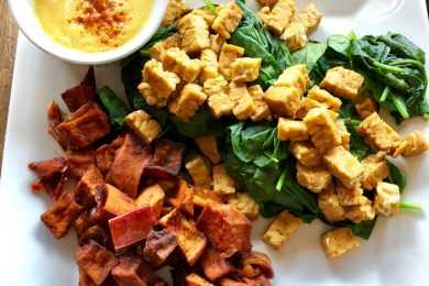 Orange and yellow Tempeh on spinach with sauce on side