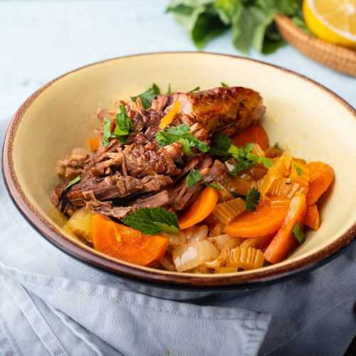 Beef brisket with sliced carrots, onion, celery and parsley in white bowl