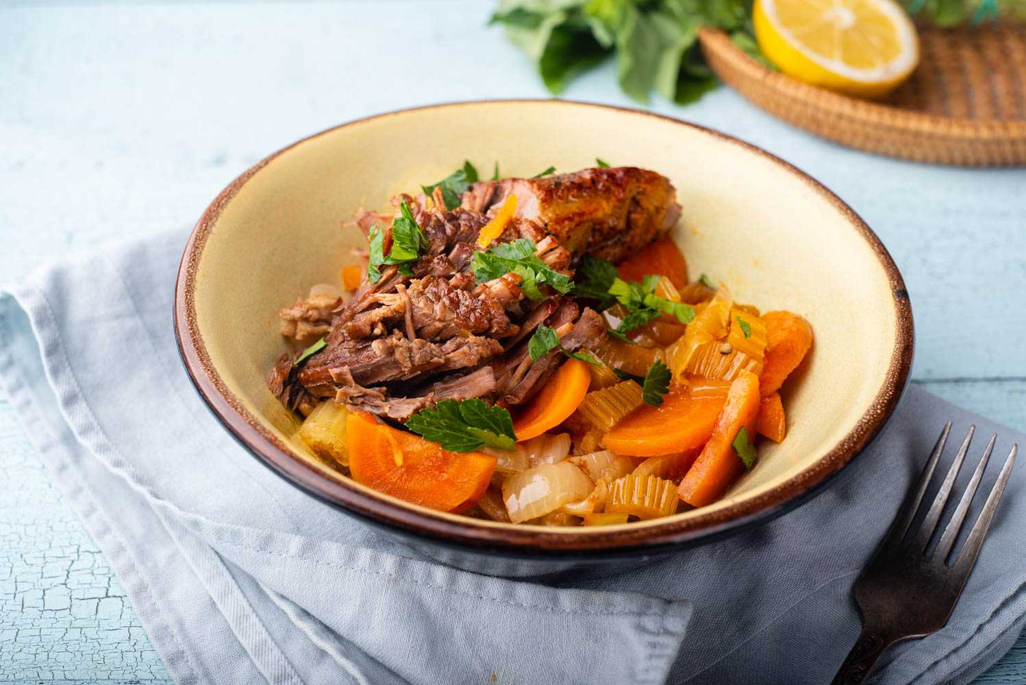 Beef brisket with sliced carrots, onion, celery and parsley in white bowl