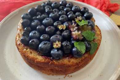 Homemade cheesecake topped with blueberries and mint leaves on a white plate