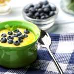 Cornmeal porridge topped with fresh blueberries in green cup with spoon and blueberries on side