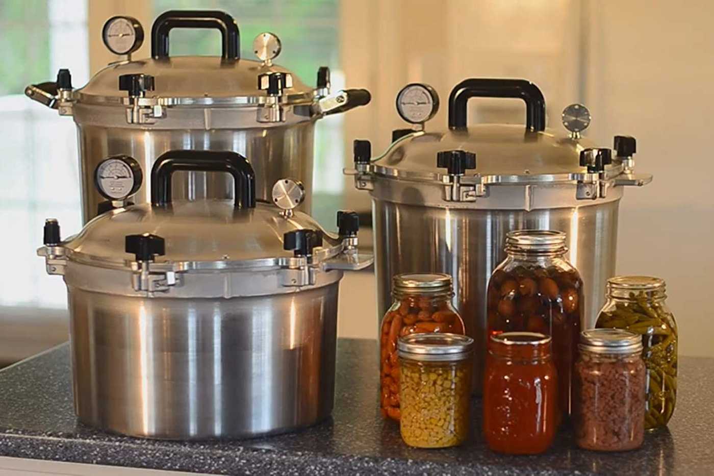 Stovetop pressure cookers with jars of pickles on a table