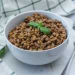 white bowl with brown lentils and milt leaves on top