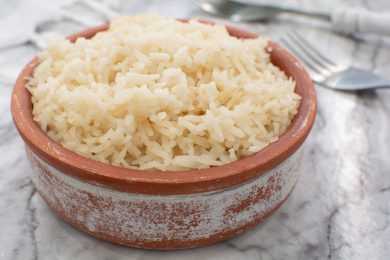Cooked jasmine rice in a brown bowl with fork on side