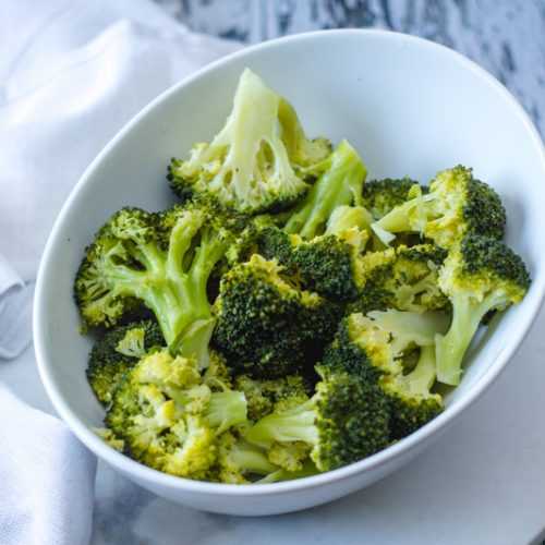 Steamed broccoli florets in white bowl top view