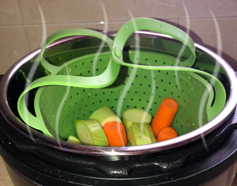 carrots and zucchini cubes inside a green steamer basket inside the Instant Pot