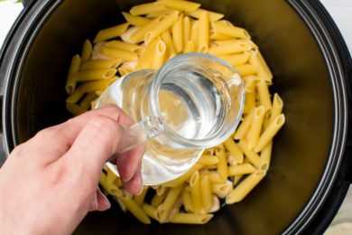 adding water from a jug into a pressure cooker filled with raw pasta