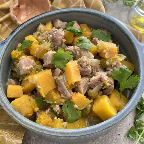 Pork loin cubes with butternut squash, parsley in green tomato and garlic sauce in blue bowl