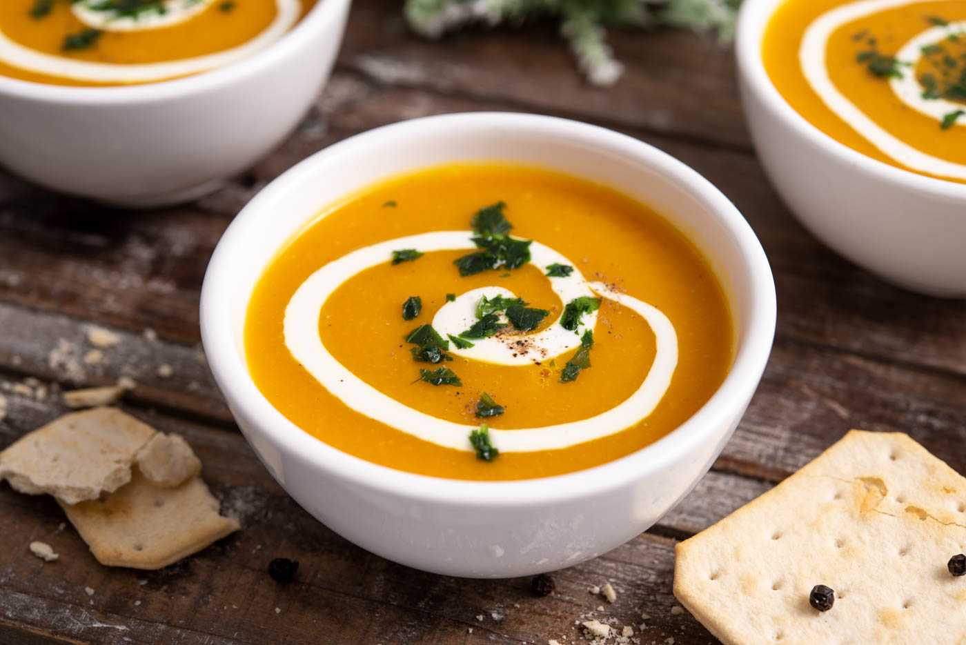 Blended Butternut squash soup in white ball topped with sour cram and chopped parsley
