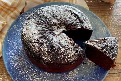 Chocolate Cake with one slice cut out topped with sugar powder on a blue plate