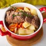 Corned beef slices over potato and carrot cubes topped with thyme in red bowl