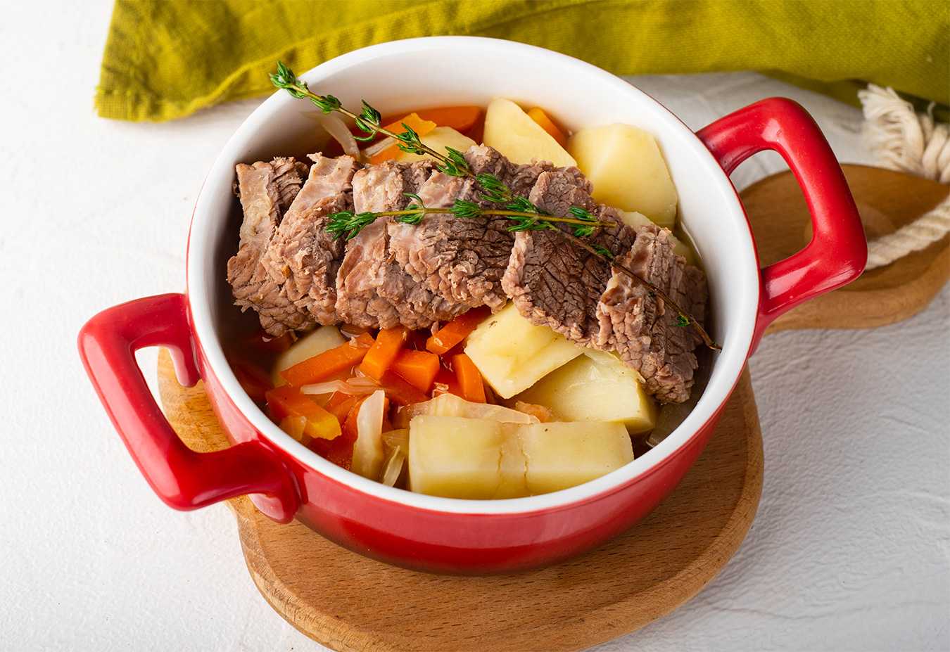 Corned beef slices over potato and carrot cubes topped with thyme in red bowl
