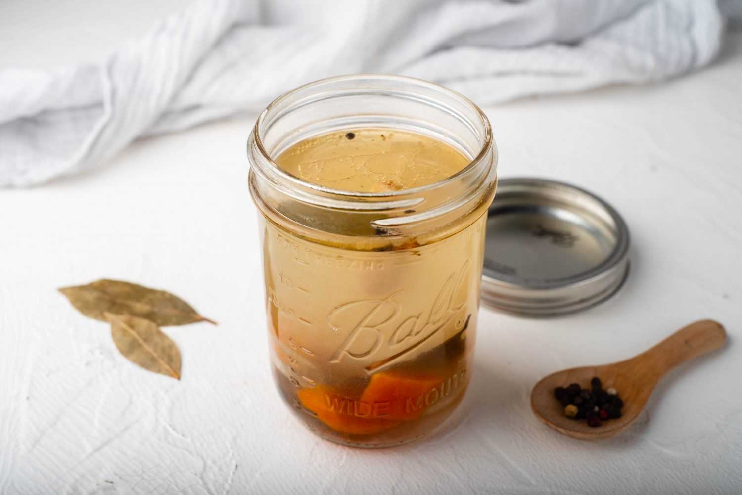 Bone broth in a jar with carrot and celery pieces on the bottom