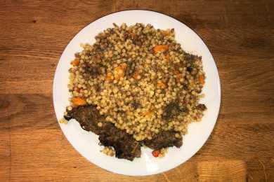 Israeli couscous mixed with ground beef, red ball peppers and carrot slices with shish kebab on side top view