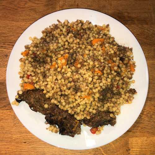 Israeli couscous mixed with ground beef, red ball peppers and carrot slices with shish kebab on side top view