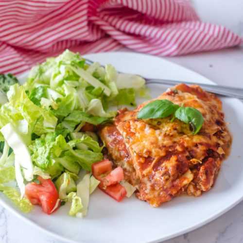 Lasagna with marinara sauce, mozzarella and parmesan cheese with lettuce and tomato salad on side