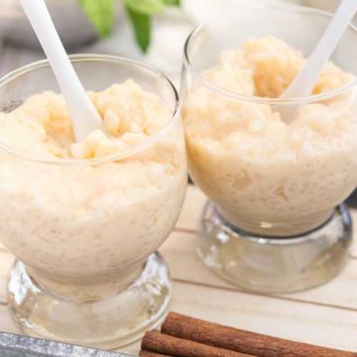 Two glasses filled with rice pudding with white spoons inside on cutter board