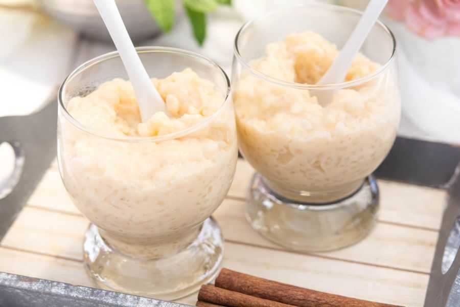 Two glasses filled with rice pudding with white spoons inside on cutter board