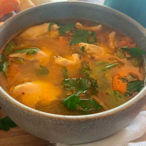 Fresh soup with salmon, carrot cubes and parsley in a grey bowl